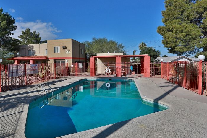 Inviting apartment complex with a crystal-clear swimming pool, surrounded by well-maintained grounds and modern buildings under a bright blue sky.