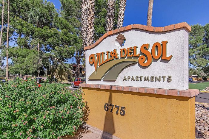Inviting entrance of Villa del Sol Apartments surrounded by lush greenery and tall trees, showcasing a warm and welcoming community.