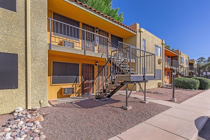 Charming apartment complex with rustic architecture and vibrant yellow facade, featuring outdoor staircases and a well-maintained landscape under a clear blue sky.