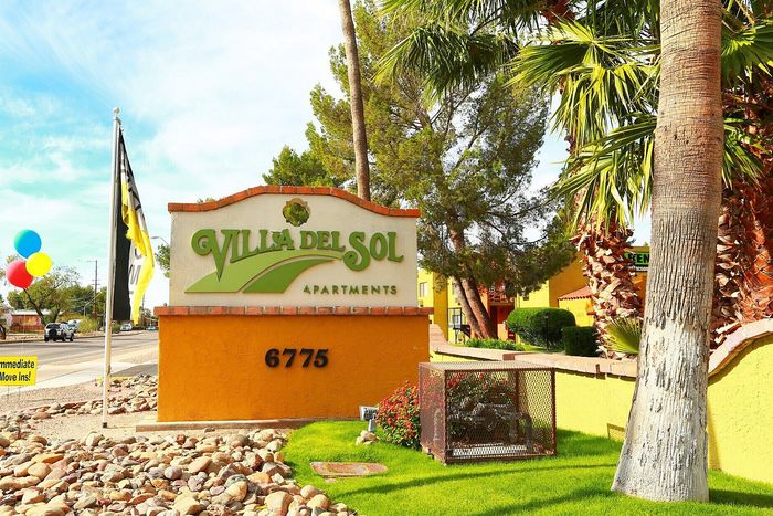 Inviting entrance to Villa Del Sol Apartments adorned with colorful balloons and lush greenery, offering immediate move-ins.