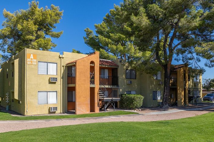 Charming apartment complex with colorful facades, surrounded by lush greenery and tall trees, featuring ample natural light and inviting entrances.