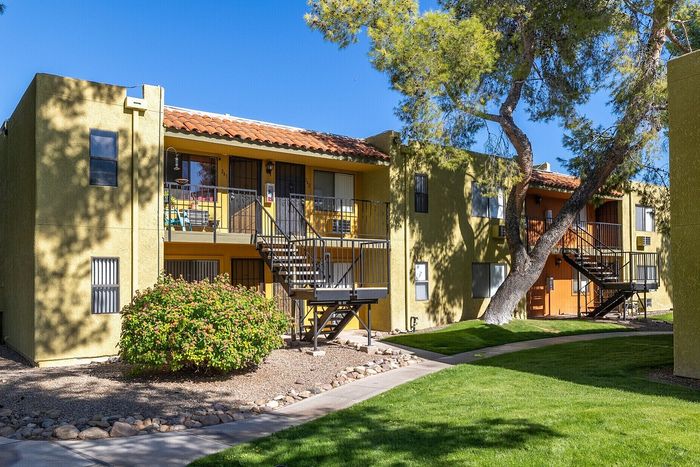 Charming apartment complex with a sunny exterior, featuring balconies and lush green landscaping.