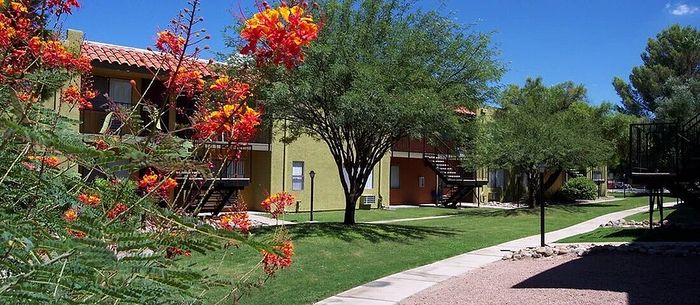 Charming apartment complex with vibrant flowering trees and well-maintained grassy areas, offering serene outdoor spaces and inviting pathways.