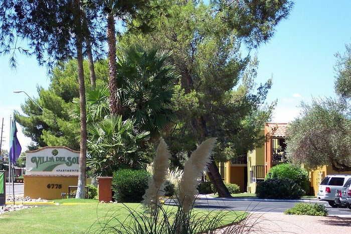 Villa Del Sol Apartments entrance surrounded by lush greenery and tall trees, offering a serene residential environment.
