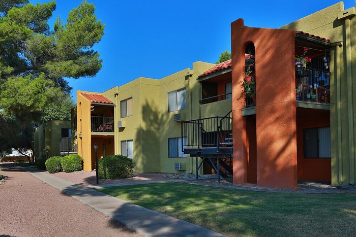 Charming apartment building with colorful stucco exterior surrounded by lush greenery and a serene walkway.