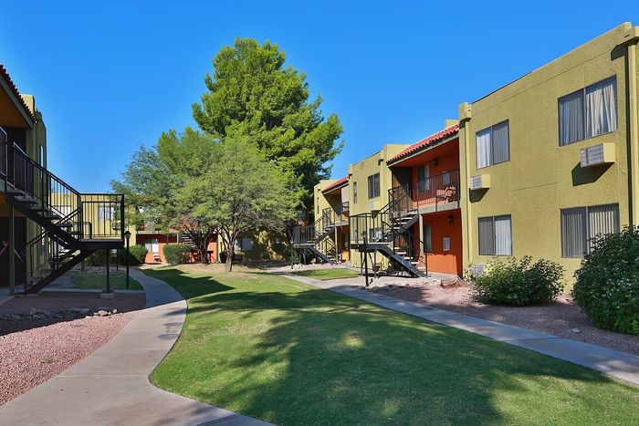 Charming apartment complex with vibrant facade, lush greenery, and inviting pathways under a clear blue sky.