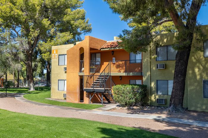 Charming apartment building with vibrant orange and green exterior, nestled among lush trees and manicured lawns, offering a serene and inviting atmosphere.
