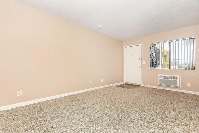 Bright and inviting room with plush carpet, light beige walls, and a stylish window offering a view of the staircase outside.