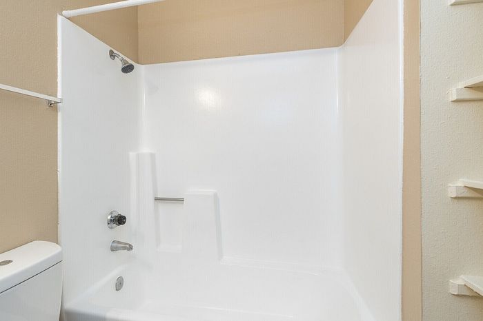 Bright and modern bathroom featuring a sleek white bathtub and shower combination with convenient shelving.