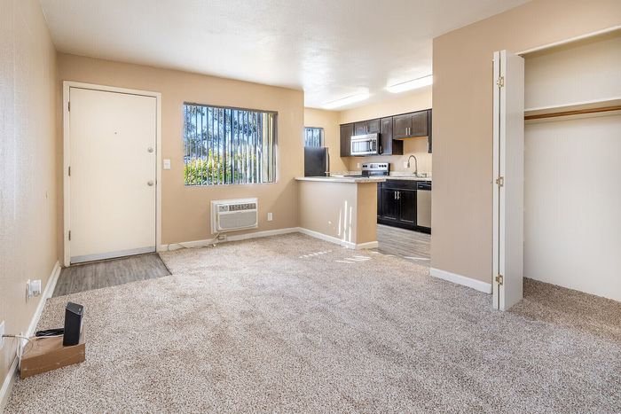 Bright and inviting living area with plush carpet, large window, and open kitchen featuring modern appliances and sleek cabinetry.