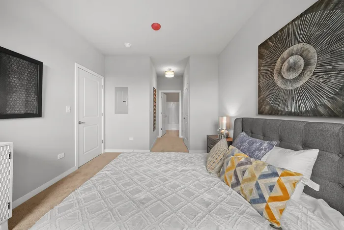 Elegant bedroom with modern decor, plush pillows, and a striking artistic wall feature, leading to a well-lit hallway.