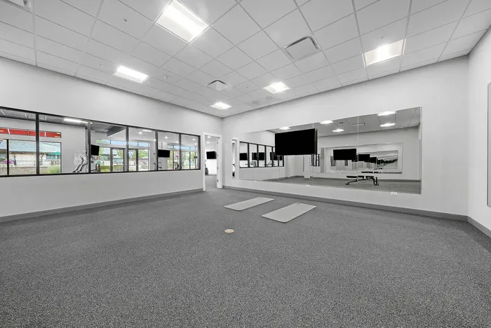 Spacious and modern fitness room featuring large mirrors, natural light, and sleek grey flooring for an invigorating workout experience.