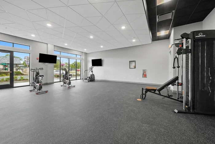 Bright and modern fitness room with large windows, exercise bikes, and strength training equipment for a dynamic workout experience.
