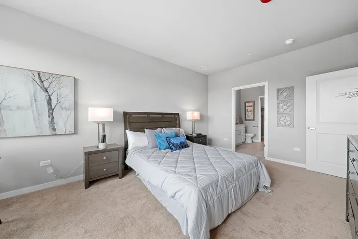 Elegant bedroom with modern decor, featuring a cozy bed with plush pillows, soft carpeting, and contemporary bedside tables, leading to an en-suite bathroom.