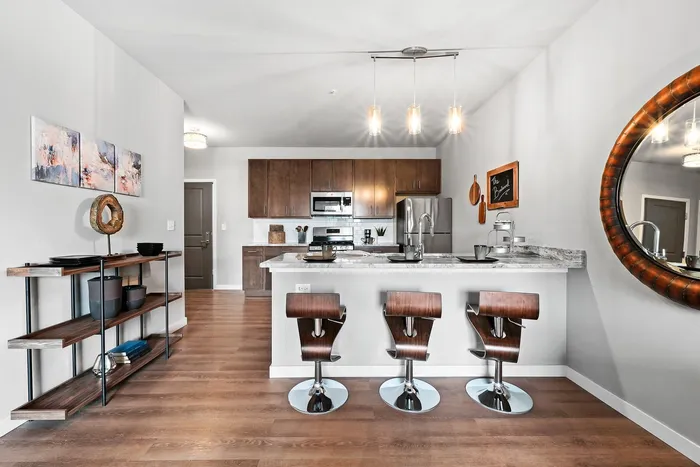 Modern kitchen with sleek marble countertops, stylish bar stools, and stainless steel appliances. Chic open shelving and artistic decor enhance the contemporary design, offering a functional and welcoming space.