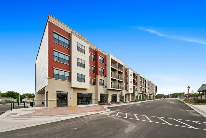 Modern multi-story apartment building with red and cream facade, ample windows, and inviting balconies, set against a vibrant blue sky in an urban setting.