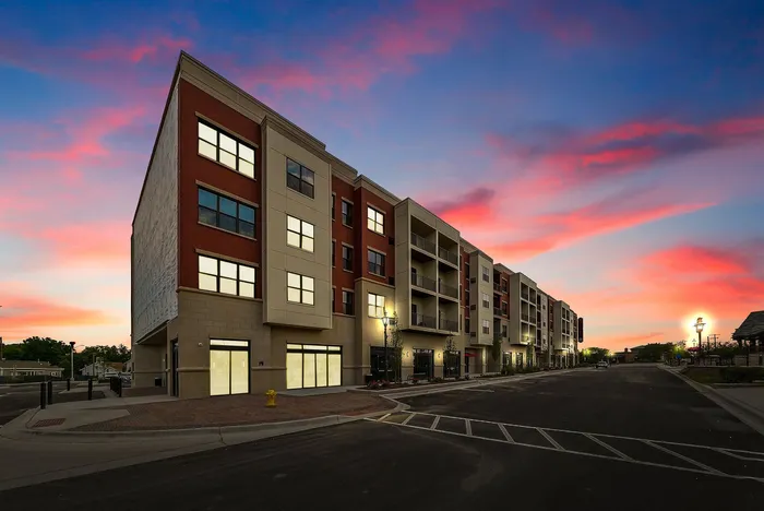 Modern apartment building exterior at sunset, featuring expansive windows and stylish facades, set in a serene urban neighborhood.