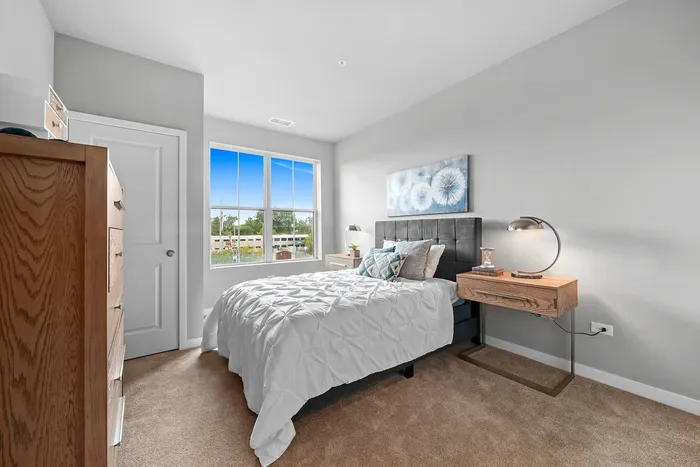 Bright and inviting bedroom with stylish decor, featuring a plush bed, modern side table, and large window overlooking a lush view.