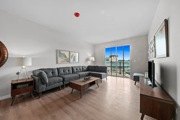Bright and modern living room featuring a stylish gray sectional, wooden coffee table, and large sliding doors opening to a scenic balcony.