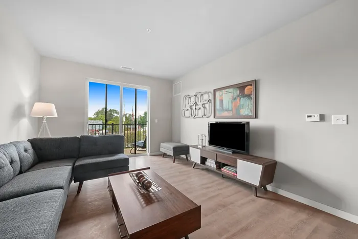 Modern living room with sleek gray sectional sofa, elegant art pieces, and a bright window view opening to a charming balcony.