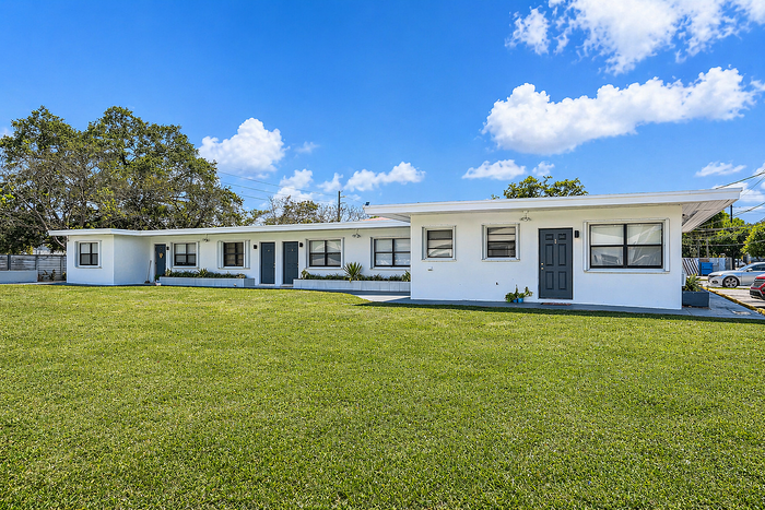 Charming white apartment complex with a well-maintained lawn, set under a bright blue sky.