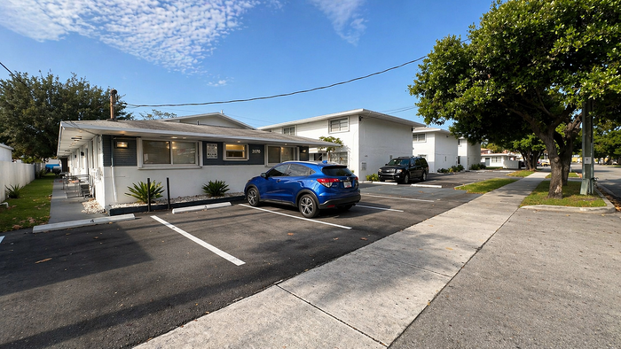 Charming apartment building with modern architecture, ample parking, and lush greenery under a clear blue sky.
