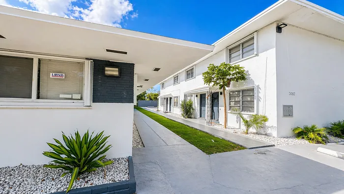 Charming apartment complex featuring modern architecture, lush greenery, and a welcoming pathway under a clear blue sky.