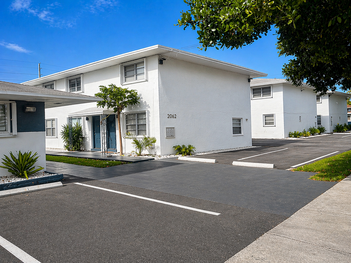 Charming two-story white apartment building with lush greenery and ample parking, perfect for modern living.