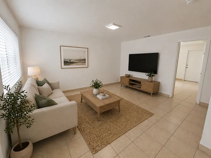 Elegant living room featuring a plush sofa, stylish coffee table, and a large wall-mounted TV, all highlighted by natural light through the window.