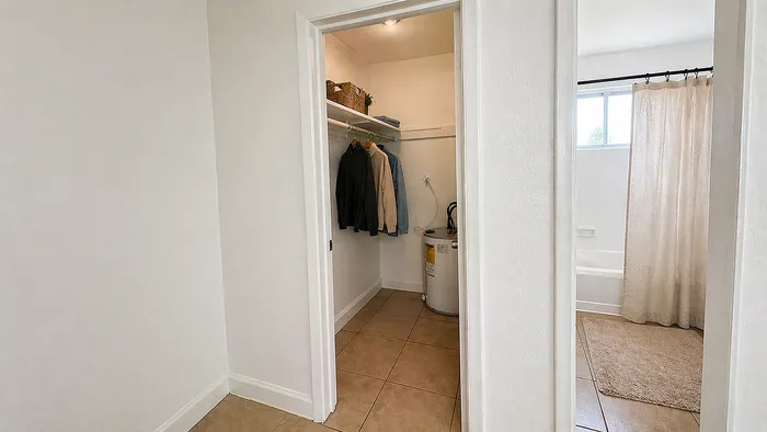 Inviting closet space featuring modern shelving and convenient storage next to a bright, airy bathroom with a large window and elegant curtain.