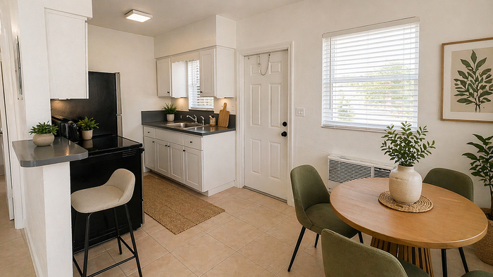Charming apartment kitchen with modern black appliances, sleek white cabinets, and a cozy dining area accented by potted plants.