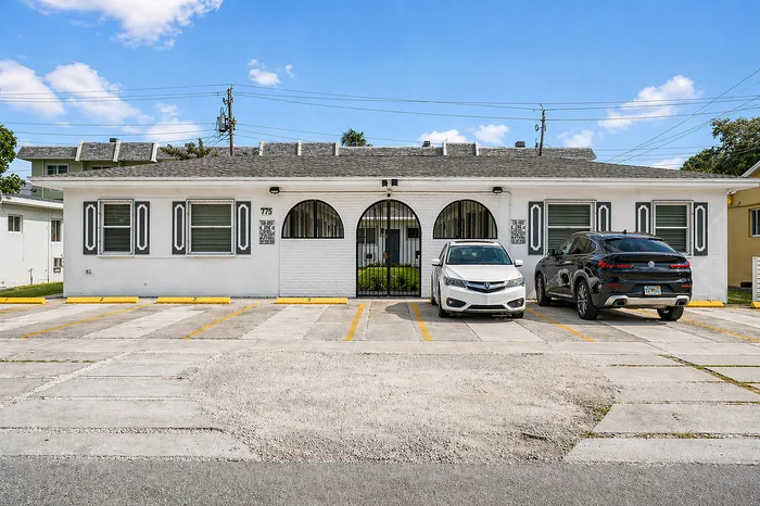 Charming single-story apartment with a white facade and arched entrances, nestled in a sunny neighborhood with convenient parking.