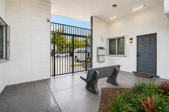 Charming apartment entryway featuring a secure gated entrance, contemporary bench seating, and lush garden accents.