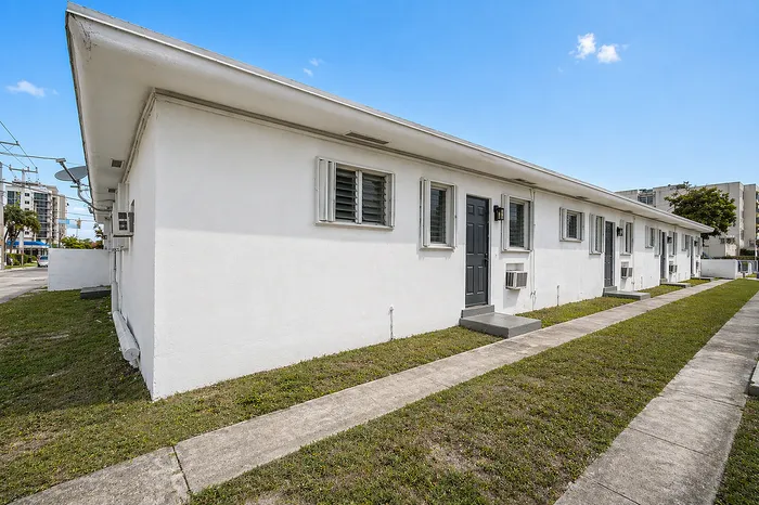 Charming row of white single-story apartments with modern design, featuring neat grassy surroundings and a clear blue sky backdrop.