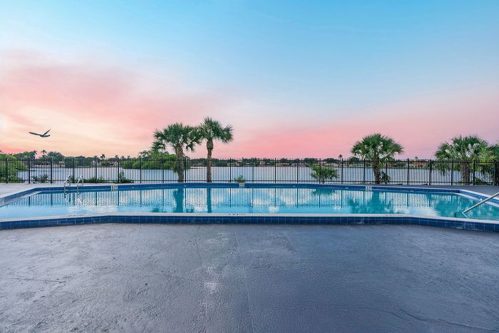Breathtaking lakeside pool with palm trees and a stunning sunset, offering a serene and picturesque backdrop.