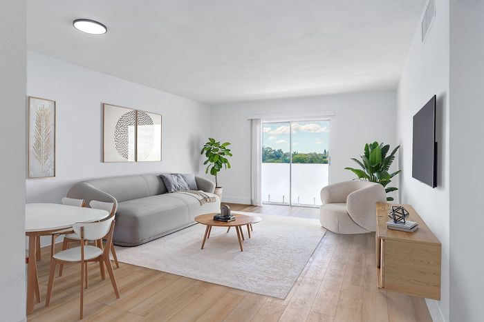 Bright and airy living room with modern furniture, featuring a cozy gray sofa, a stylish armchair, and a sleek wooden coffee table against a backdrop of large glass sliding doors with a scenic view.