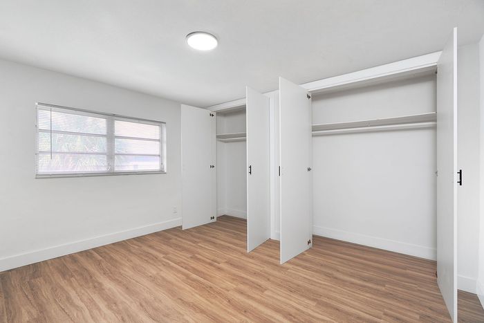 Bright bedroom with sleek wood flooring and spacious built-in closets, featuring a large window for natural light.