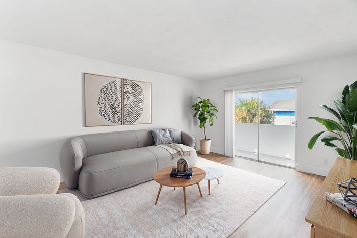 Bright and stylish living room with a sleek grey sofa, modern decor, and lush plants near a large sliding glass door leading to a serene outdoor view.