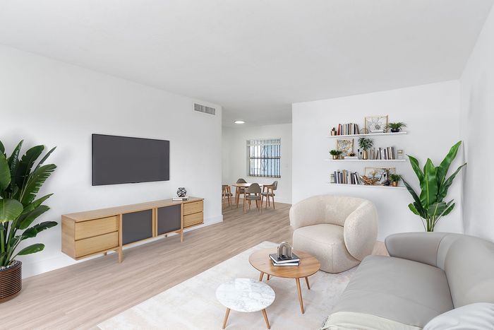 Modern living room with sleek furnishings, lush green plants, and a cozy seating area leading to a serene dining space.