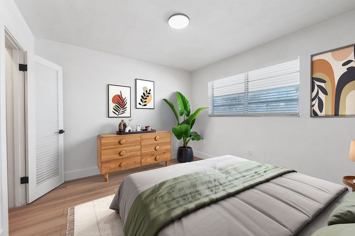 Inviting bedroom with modern decor, featuring a wooden dresser, lush green plant, and vibrant abstract artwork.