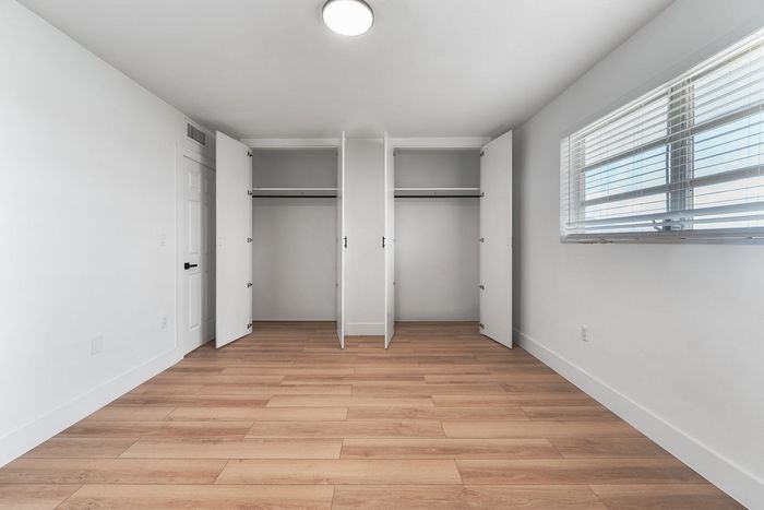 Bright and spacious bedroom featuring elegant hardwood flooring, ample closet space, and abundant natural light through large windows.