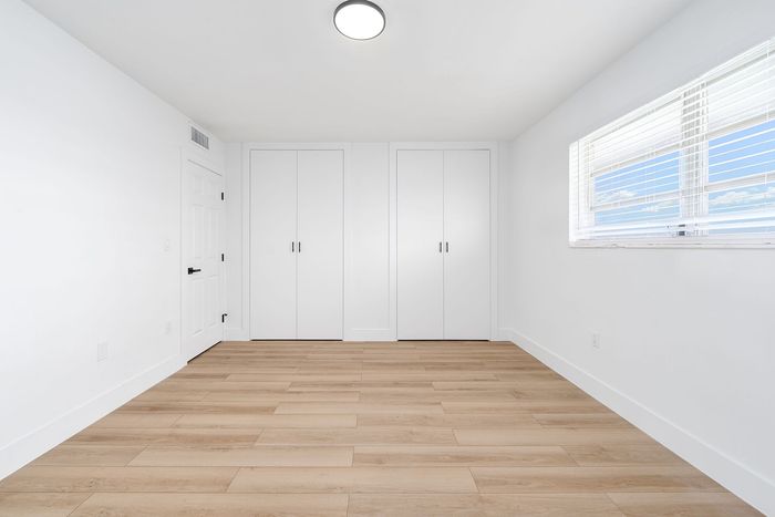 Bright, spacious room with sleek hardwood floors and abundant natural light from a large window, featuring modern double closets for ample storage.