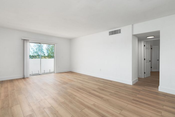 Spacious living area with elegant wood flooring, abundant natural light from large sliding glass doors, and a welcoming neutral palette.