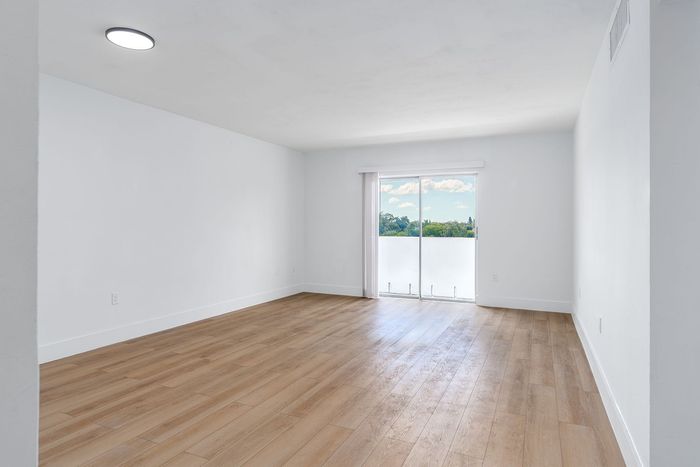 Bright and spacious living room with sleek wood flooring and large sliding glass doors leading to a balcony with scenic views.
