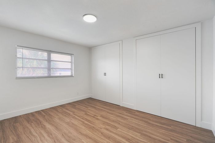 Bright, minimalist room with large window and ample closet space, featuring sleek wood flooring and modern design.