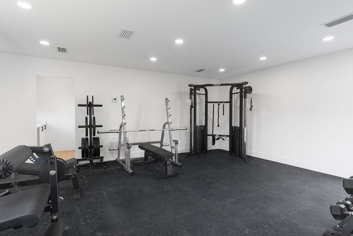 Modern fitness room with high-quality gym equipment including weights and a training bench in a bright, spacious setting.