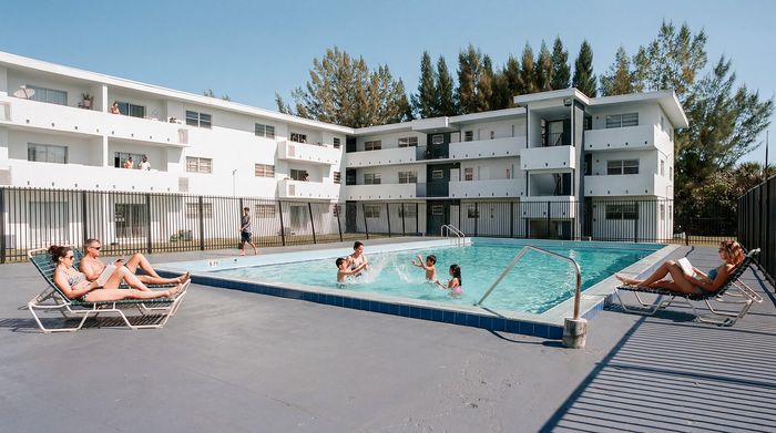 Inviting apartment complex with a sparkling swimming pool, surrounded by lounging residents and lush greenery, perfect for relaxation.