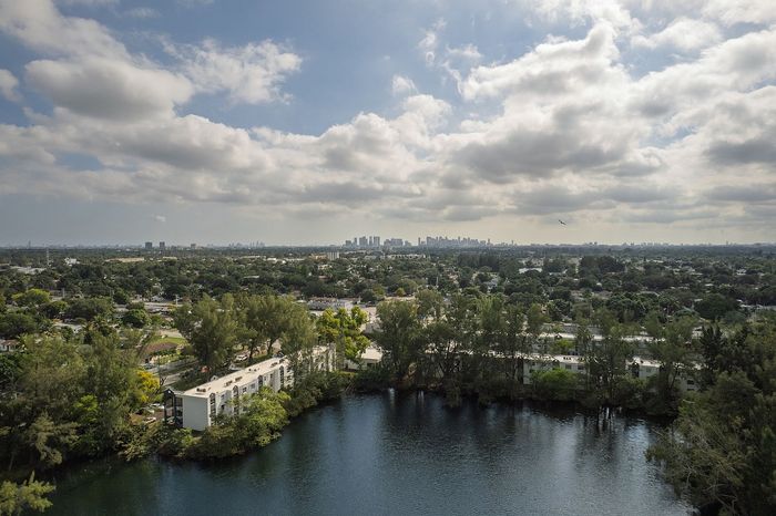 Panoramic view of lush greenery surrounding a serene lake with a distant city skyline under a vibrant cloudy sky.