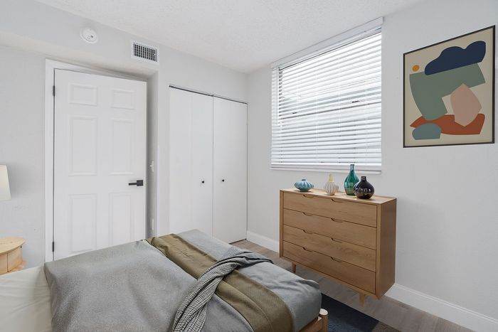Bright, modern bedroom with sleek white walls, stylish wooden dresser, and contemporary abstract artwork.