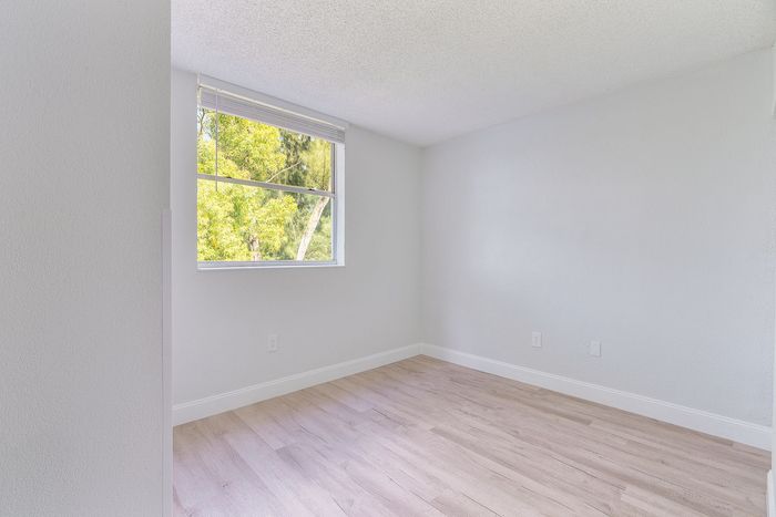 Bright and inviting room with stylish wood flooring and a large window overlooking a lush green view.